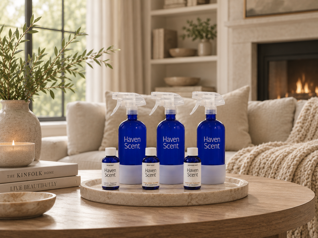 Four Haven Scent home fragrance bottles in blue and white glass, including two spray bottles and two small diffusers, arranged on a round marble tray on a wooden coffee table in a cozy living room setting.